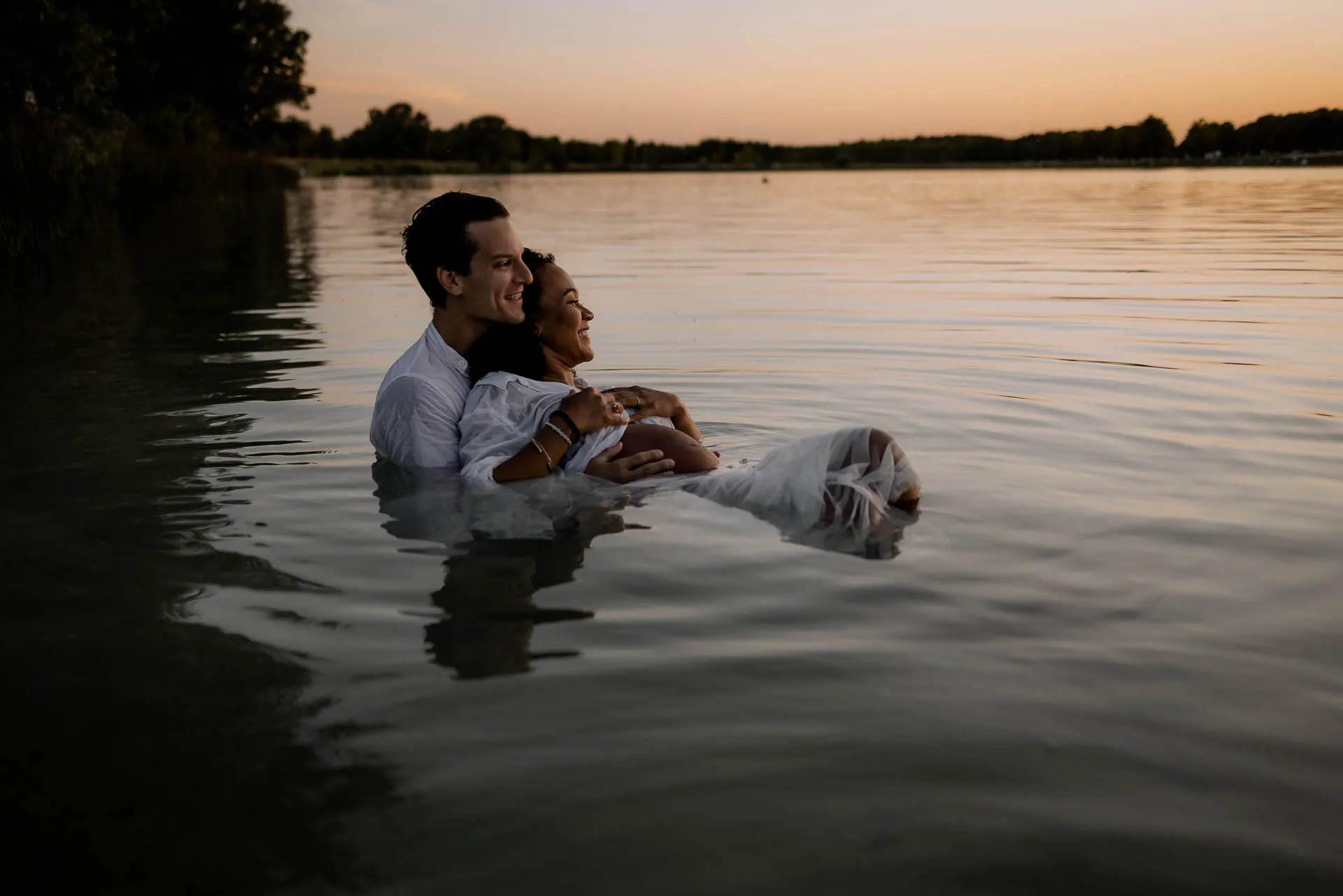 Schwangeres Paar umarmt sich im Wasser bei Sonnenuntergang Babybauchshooting München