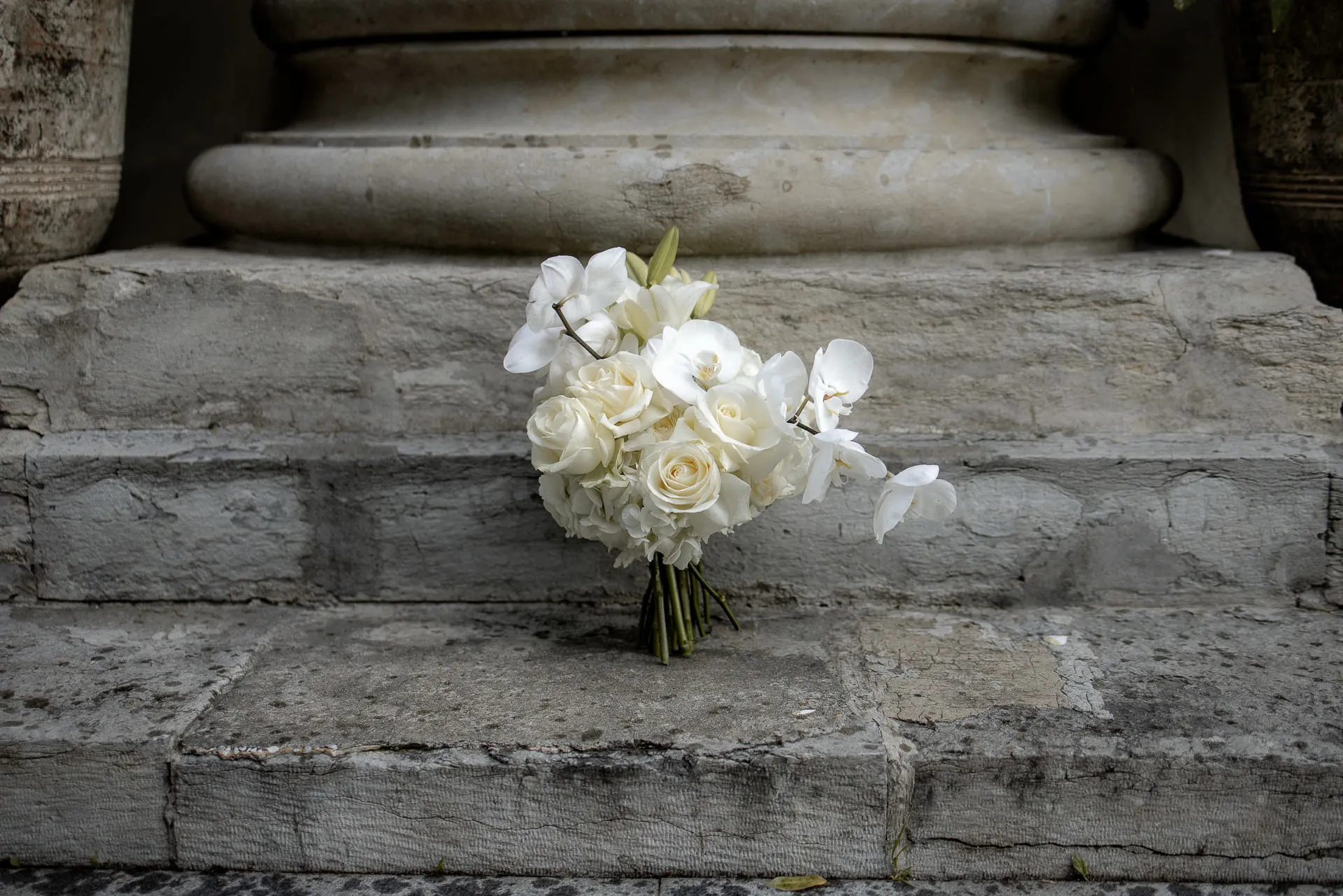 Eleganter Brautstrauß mit weißen Rosen und Orchideen auf antiker Treppe