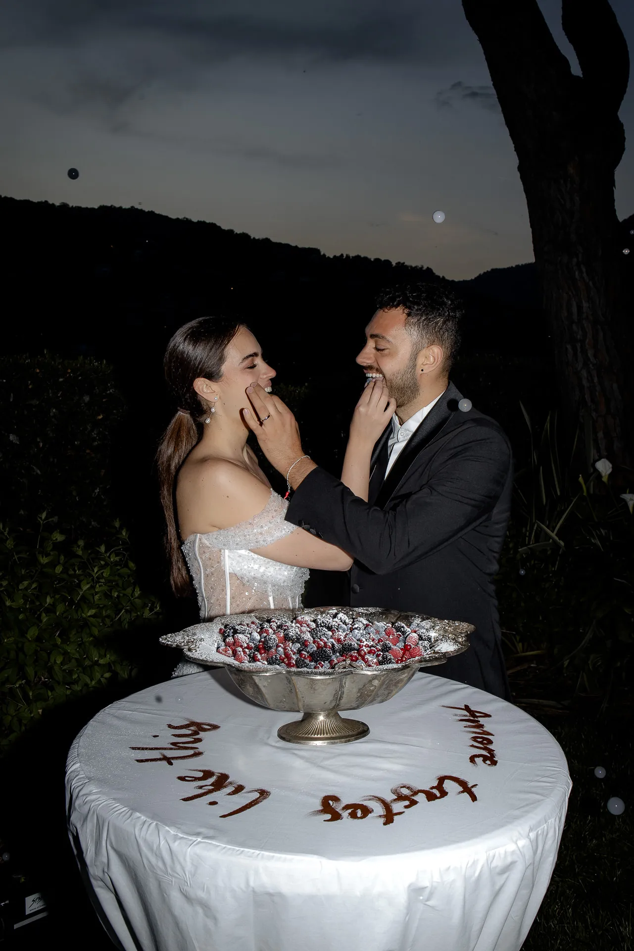 Brautpaar füttert sich gegenseitig Hochzeitstorte bei Nacht am Comer See