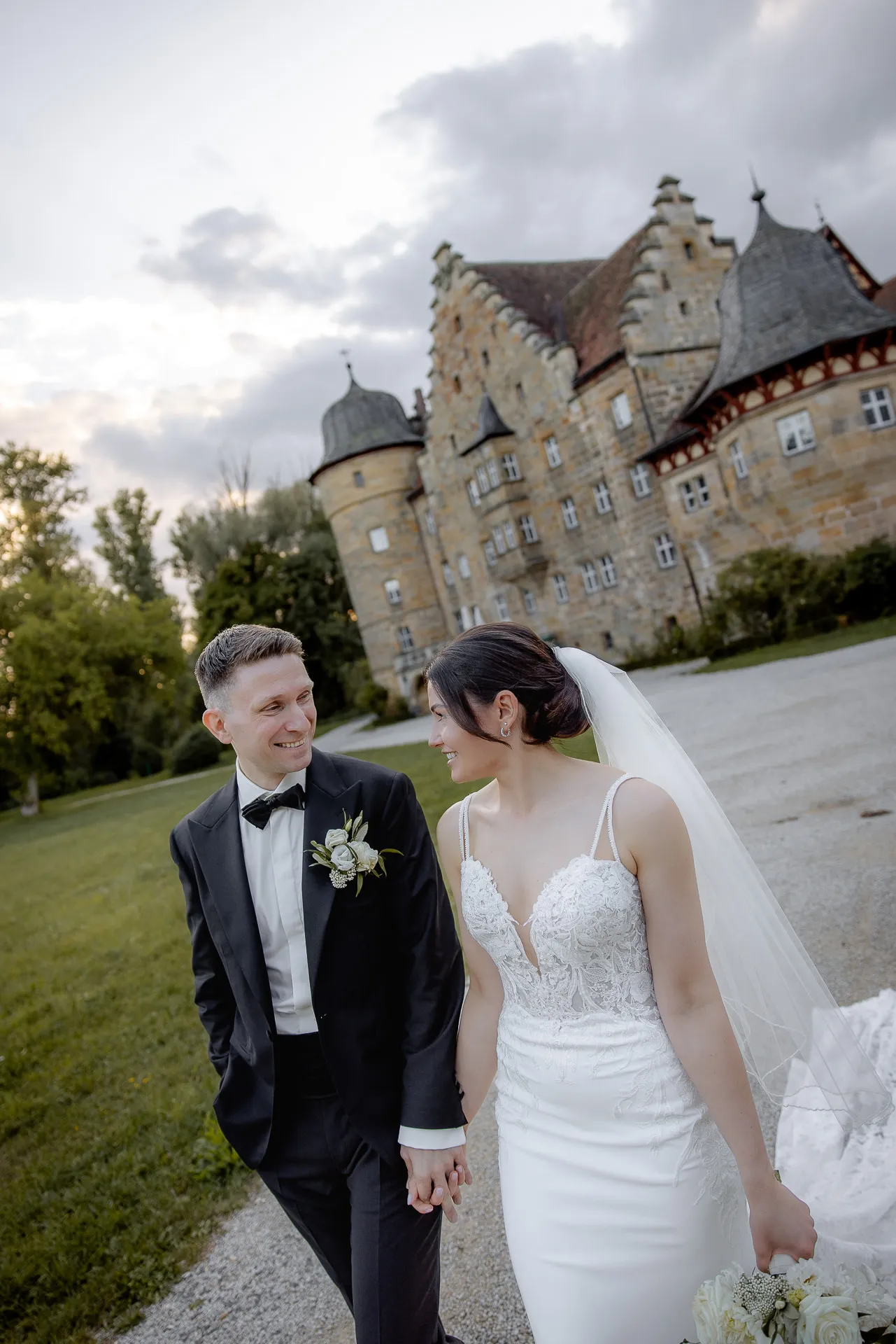 Glückliches Brautpaar vor imposantem Schloss Eyrichshof bei Abendhochzeit mit dramatischem Himmel