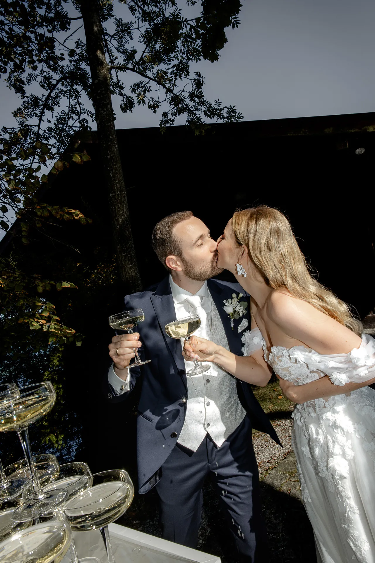 Brautpaar küsst sich mit Champagnergläsern nach Champagnerpyramide