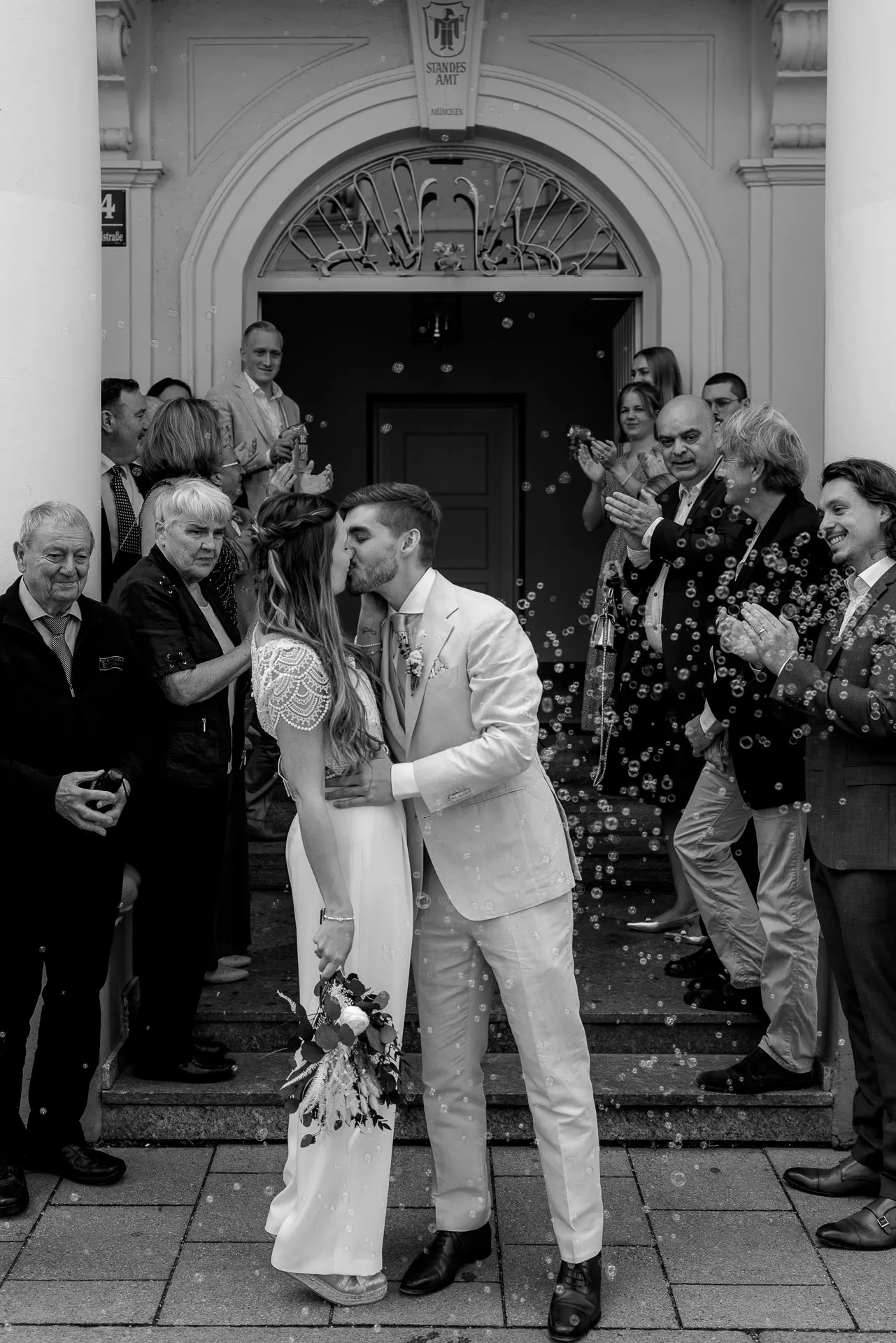 Brautpaarkuss vor Standesamt Mandlstraße mit Gästen – emotionale Hochzeitsfotografie