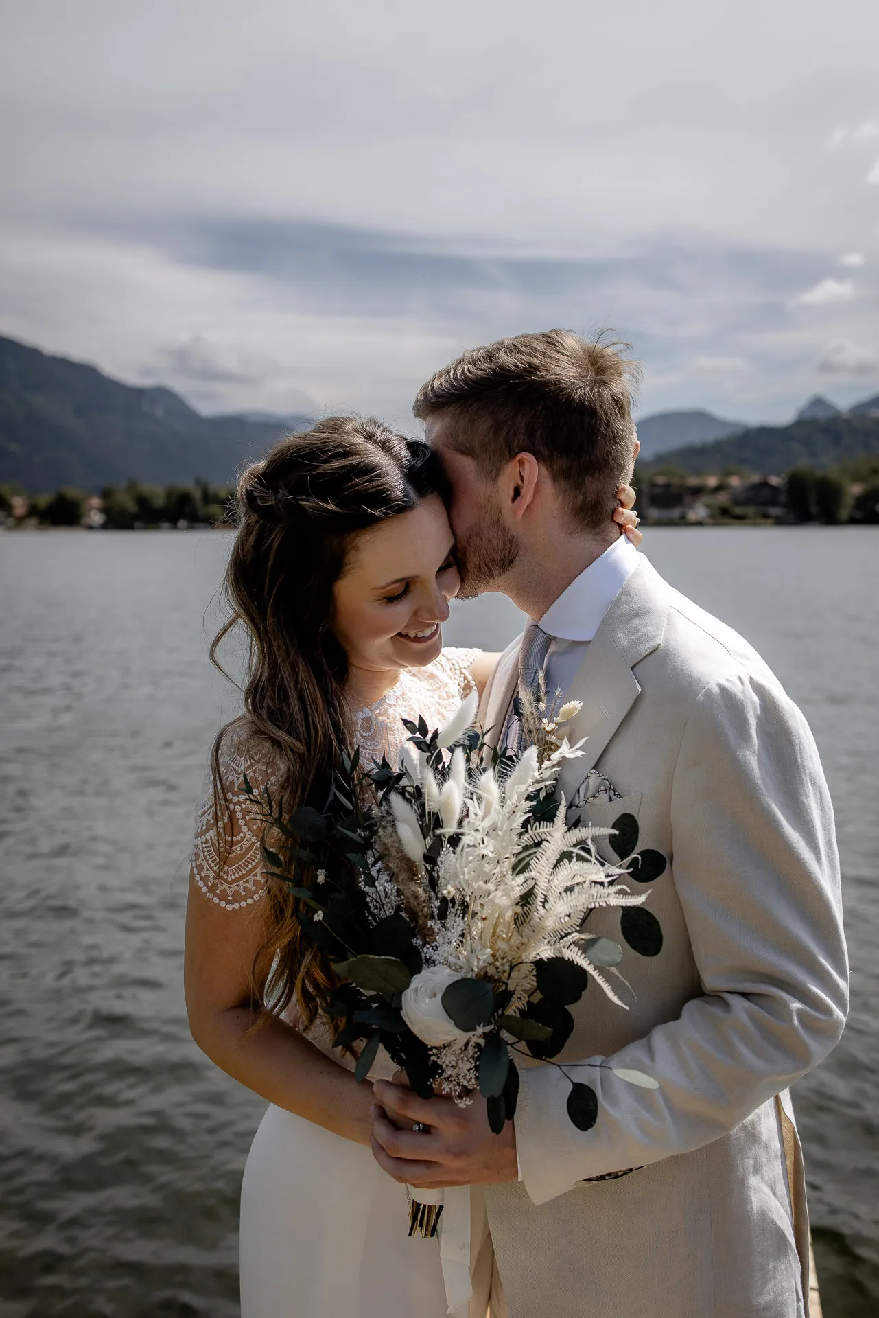 Romantischer Brautpaarkuss am Tegernsee mit Boho-Strauß – emotionale Hochzeitsfotografie