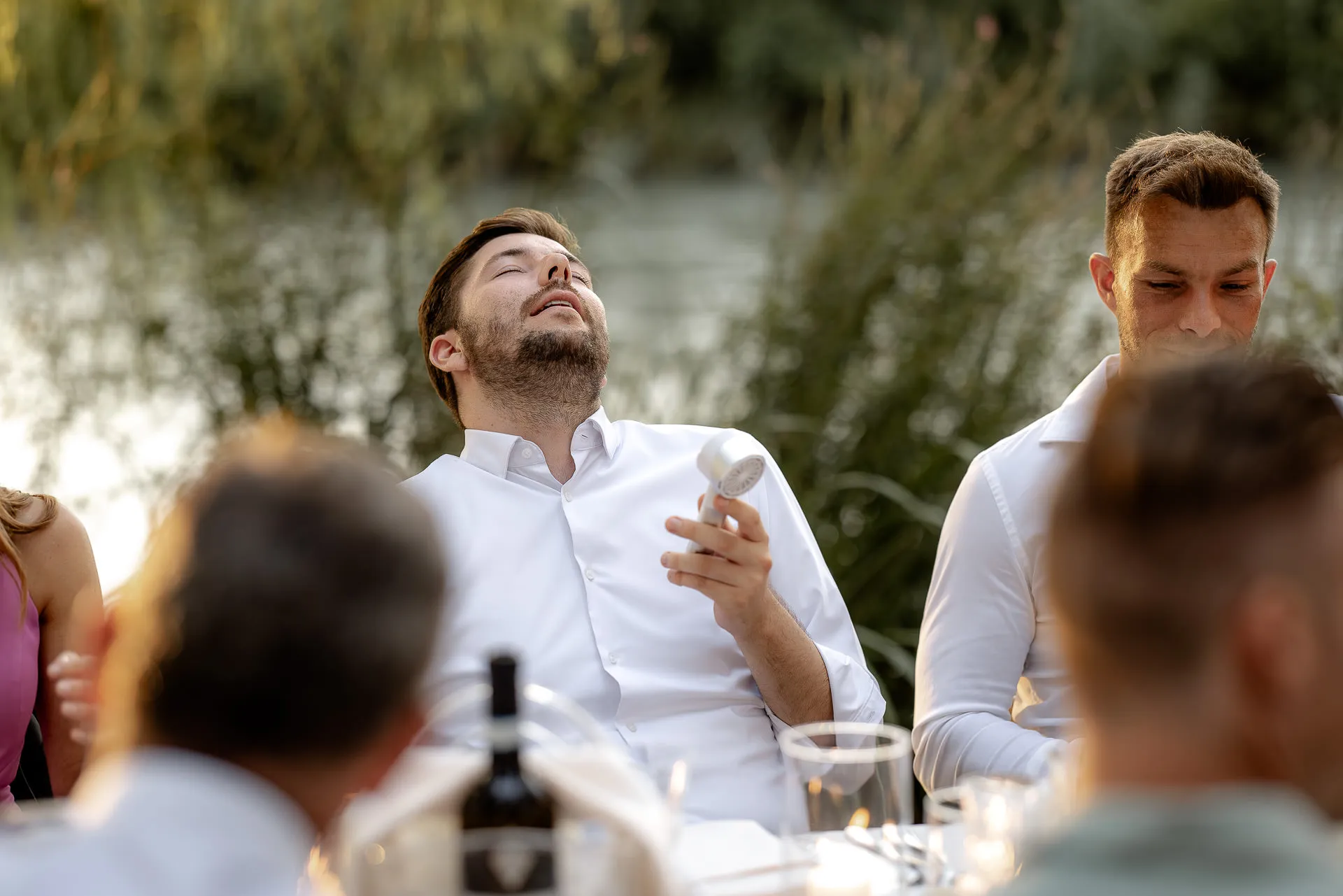 Lachender Hochzeitsgast genießt ausgelassene Feier am Fluss bei goldener Abendsonne