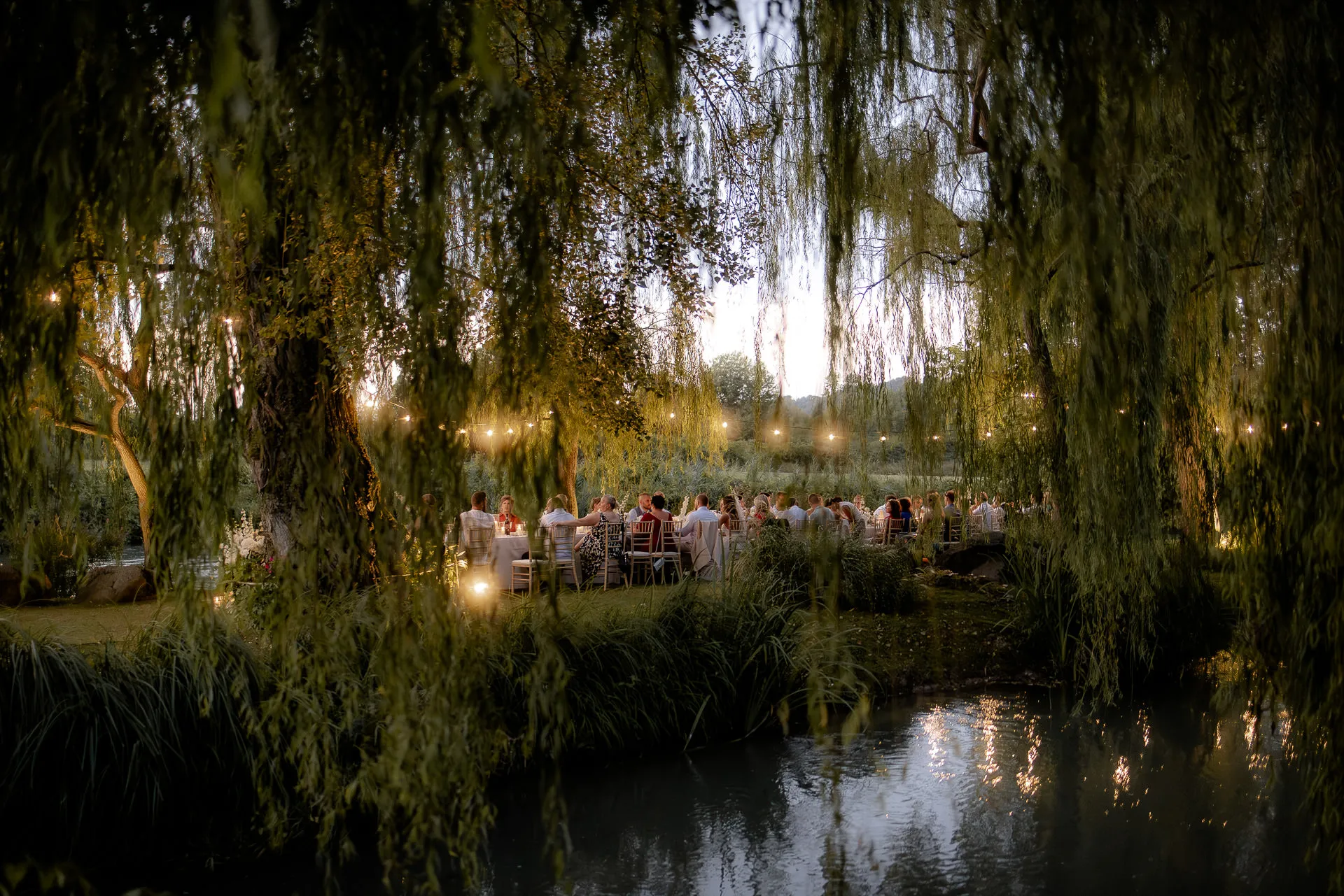 Zauberhafte Abendhochzeit am Fluss mit Lichterketten unter Weiden bei La Finestra