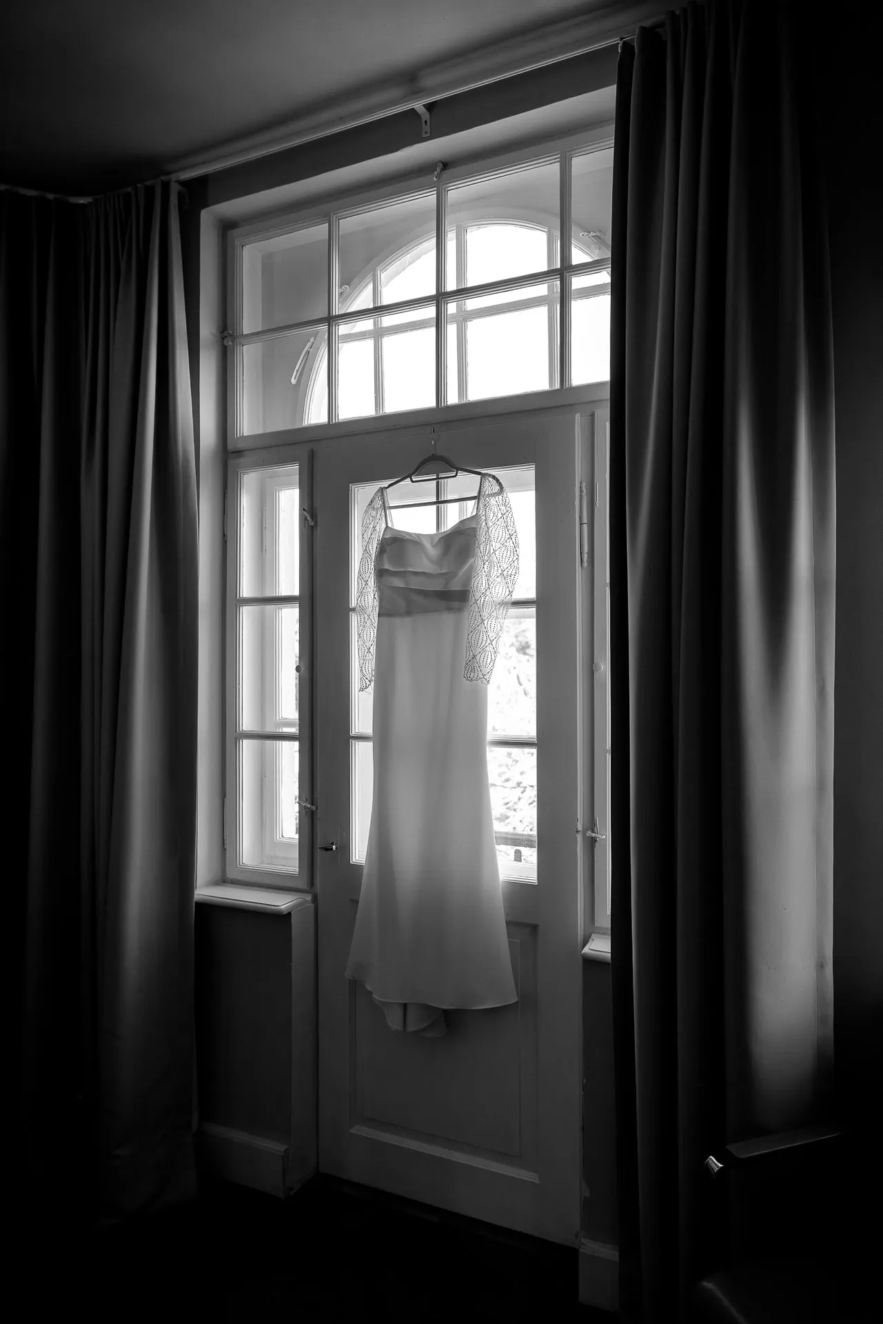 Brautkleid hängt am Fenster in Schwarz-Weiß bei Gut Sonnenhausen Hochzeit