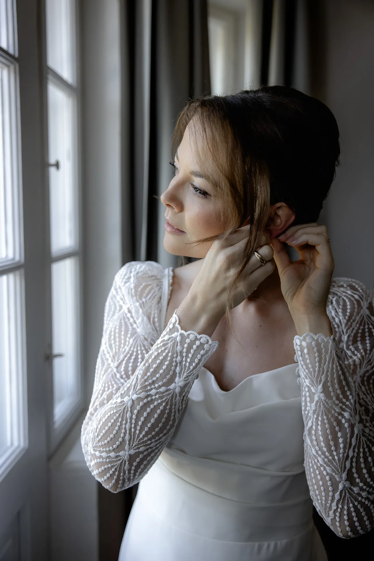 Braut legt Ohrringe an am Fenster bei Gut Sonnenhausen Hochzeit