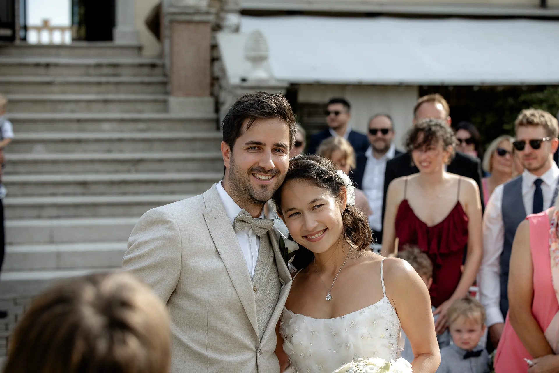 Strahlendes Brautpaar nach der Trauung mit Gästen im Hintergrund