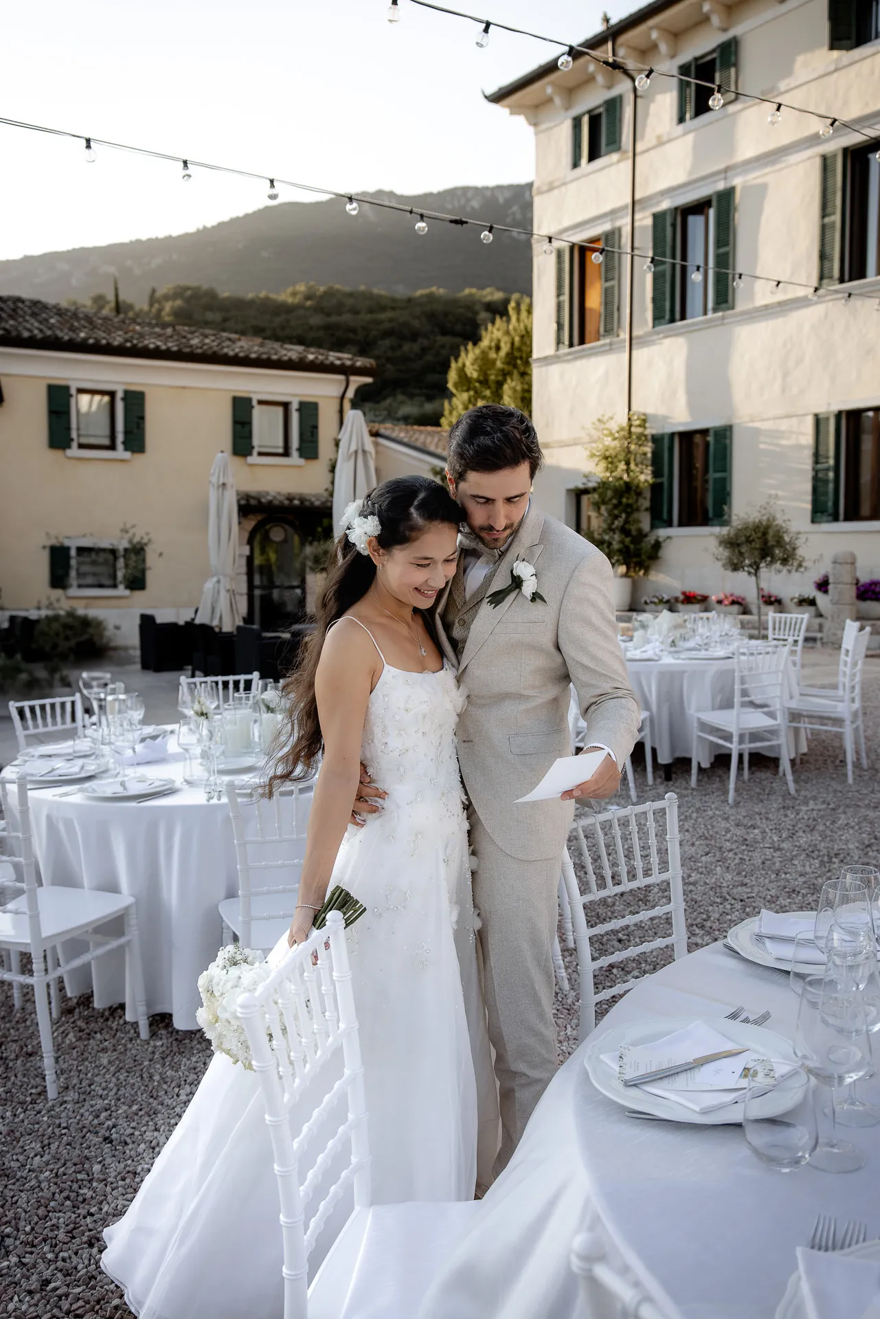 Verliebtes Brautpaar zwischen weißen Tischen mit Bergpanorama in der Villa Cariola